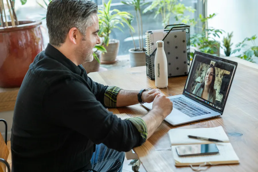 A man smiles during a video call on his laptop at a sunny desk